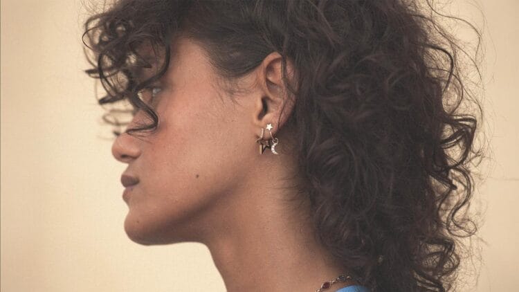 Une femme aux cheveux bouclés porte des boucles d'oreilles dorées en forme d'étoile et de lune.